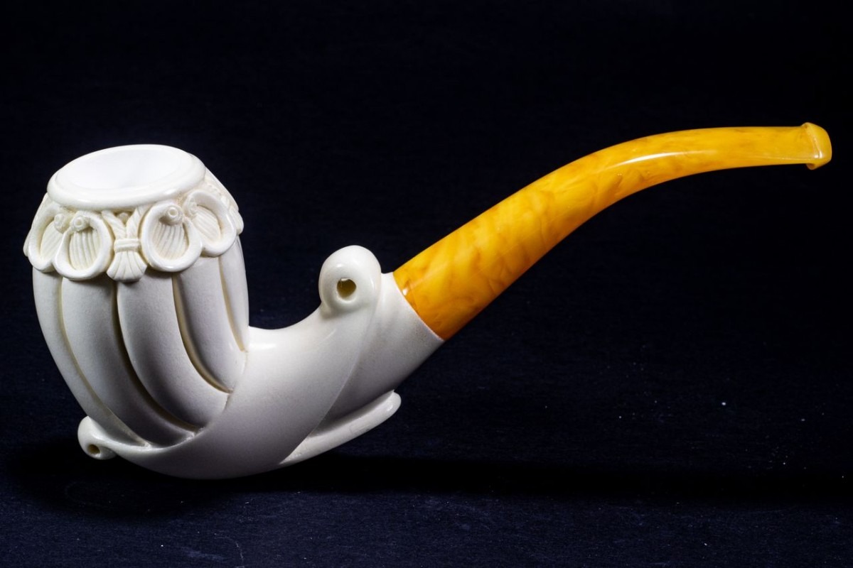 Artistic Meerschaum Free Form pipe with elegant shell-inspired carvings and a curved amber stem, shown on a black background.